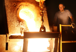 Foundry employee pours molten iron into mold for casting.